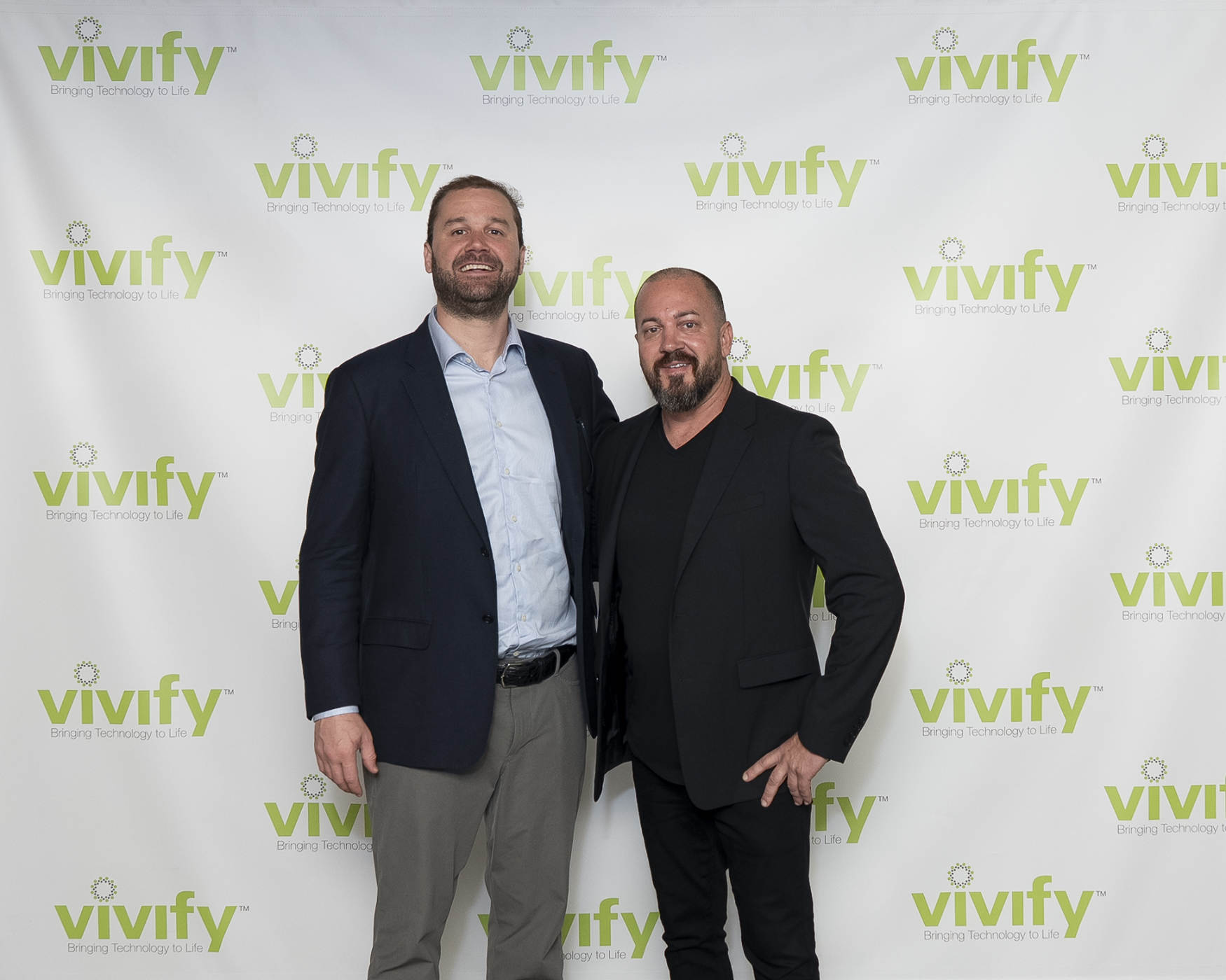 Two men standing together in front of a VIVIFY Technology backdrop